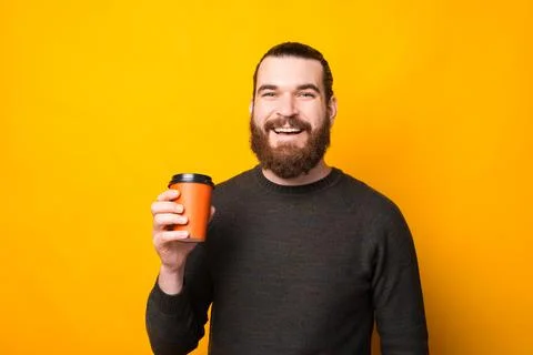 Cheerful handsome bearded man drinking cup of coffee take away over yellow 스톡 사진