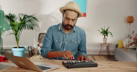 Cheerful Hispanic man creating music using silver laptop and midi controller at Stock Footage 120744503
