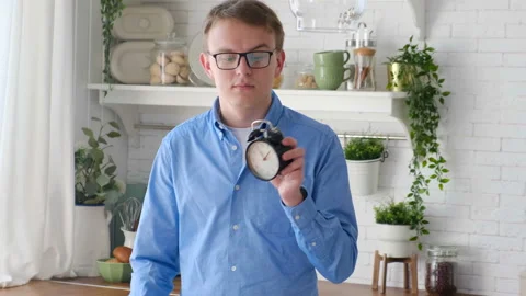 Cheerful hungry man with a clock in the kitchen showing while eating Stock Footage 127686284