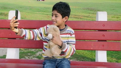 A cheerful kid using his smartphone to click a selfie with his teddy bear whi... Stock Footage 169982758