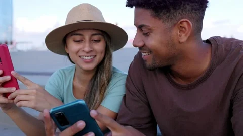 Cheerful latin couple using mobile phones sitting outdoors. Stock Footage 263540828