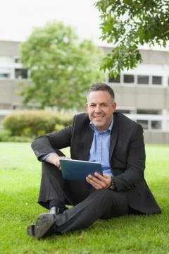 Cheerful lecturer using his tablet pc sitting outside on campus Photos