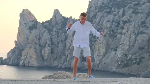 Cheerful man dancing on the background of mountains and sea Stock Footage 157818410