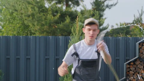 Cheerful man dancing with a garden hose, dousing himself with water Stock Footage 276363778