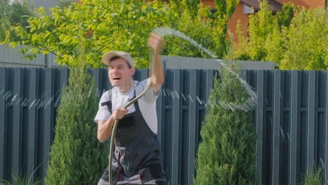 Cheerful man dancing with a garden hose, dousing himself with water Stock Footage 276419035