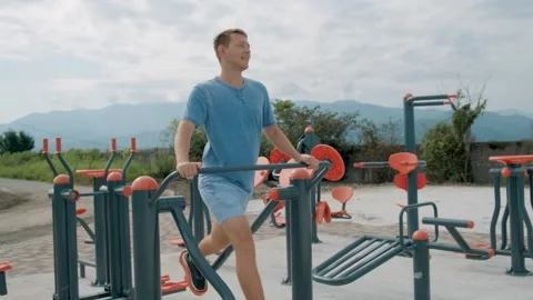 Cheerful man doing cardio workout exercises on elliptical trainer in a street Video stock 248997792