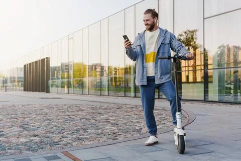 Cheerful man with e-scooter using scooter-sharing system application on hi... Stock Photos