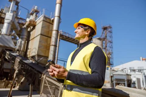 Cheerful man engineer using smartphone at industrial site Stock Photos