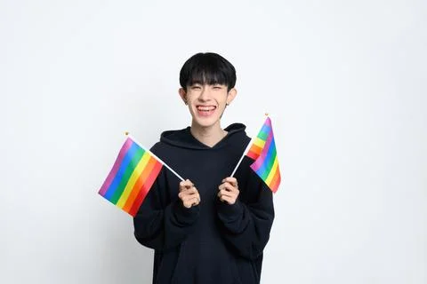 Cheerful man holding two small rainbow pride flags against white background Stock Photos