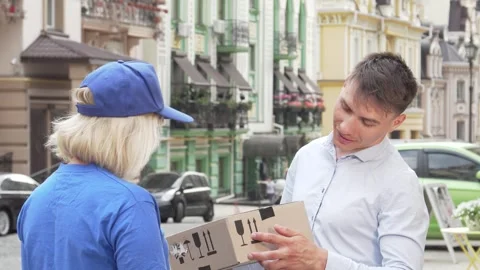 Cheerful man receiving package from friendly female courier in urban setting Stock Footage 311984218