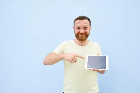 Cheerful man with a red beard points at the tablet, space for text. Stock Photos