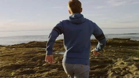 Cheerful man is running on a beach and raising his hands up to the sun Stock Footage 75746515