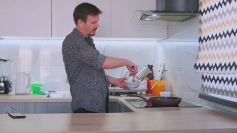 Cheerful man singing and dancing while whisking eggs for an omelet in kitchen Stock Footage 317279240
