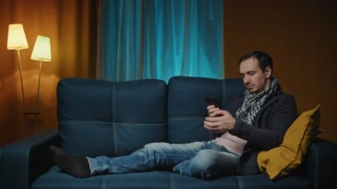 Cheerful man on the sofa using phone smile in the modern apartment texting Stock Footage 172094424