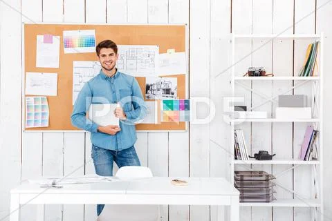 Cheerful man standing at the task board and holding laptop Stock Photos