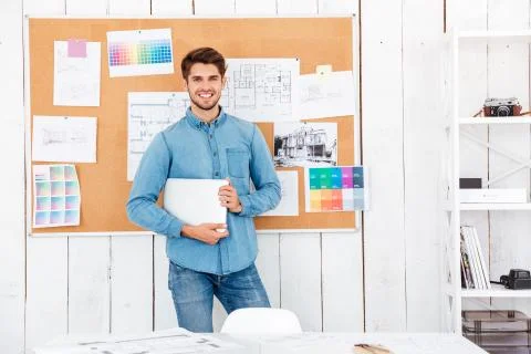 Cheerful man standing at the task board and holding laptop Stock Photos