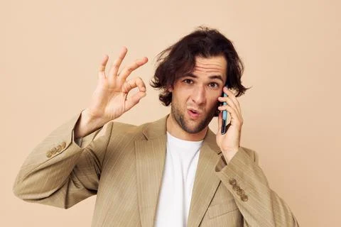Cheerful man in a suit posing emotions talking on the phone beige background Stock Photos