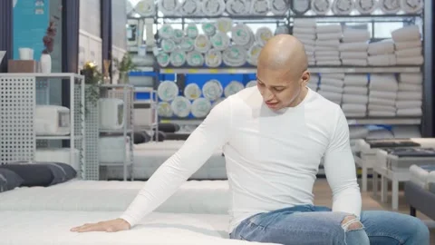 Cheerful man testing a comfortable mattress at a furniture store Stock Footage 311985449