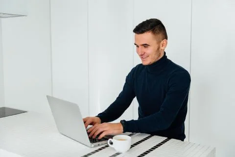 Cheerful man using a laptop while sitting for the table with cup of tea Stock Photos