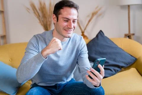 Cheerful man using smartphone on sofa has a great news Stock Photos