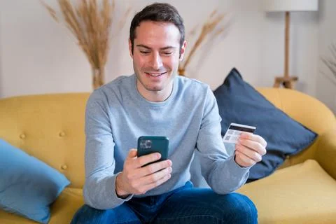 Cheerful man using smartphone on sofa shopping online Stock Photos