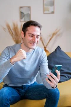 Cheerful man using smartphone on sofa has a great news Stock Photos