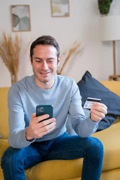 Cheerful man using smartphone on sofa shopping online Stock Photos