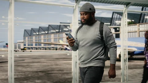Cheerful man walking in airport, using mobile phone to send texts Stock Footage 336669387