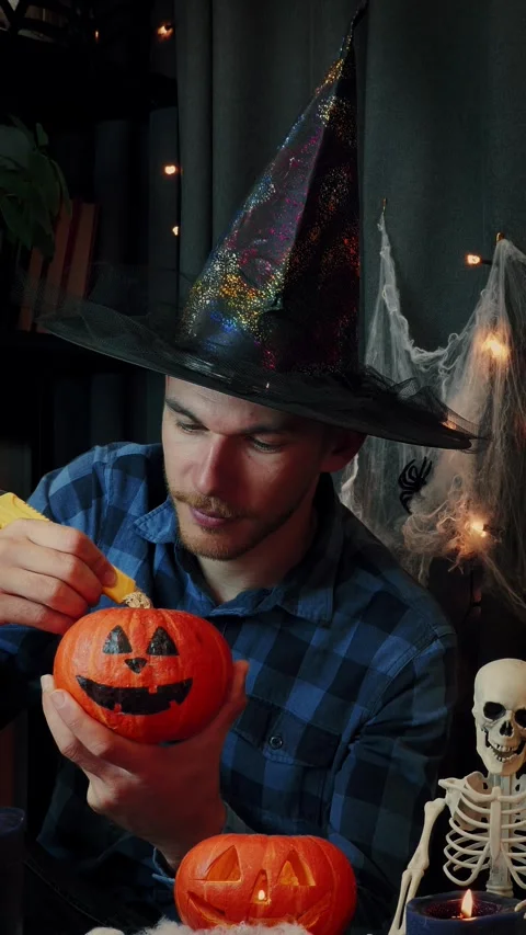 Cheerful man in witch hat carving pumpkin for Halloween party. Vertical video Stock Footage 317198359
