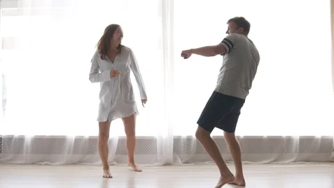Cheerful married couple dancing in their pajamas by the window in the morning Stock Footage 112600790