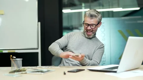 Cheerful mature gray haired bearded businessman happily scatters dollar bills at Stock Footage 232575113