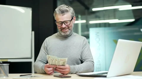 Cheerful mature gray haired bearded businessman in glasses counts dollar bills a Stock Footage 232575163
