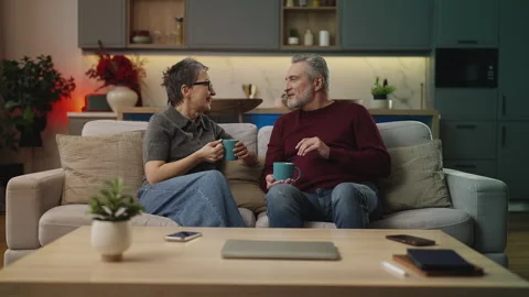 Cheerful middle-aged couple talking and drinking tea at home, warm relationship Stock Footage 340919581