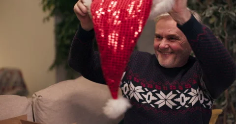 Cheerful middle-aged man with gray hair takes Santa's hat out of the box and Stock Footage 210603106