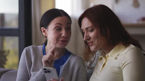 Cheerful middle-aged women browsing a dating app on a smartphone, having fun Stock Footage 337948288