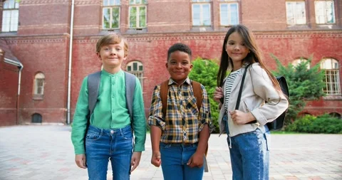Cheerful mixed-races junior students with school bags standing in front of Stock Footage 138054111