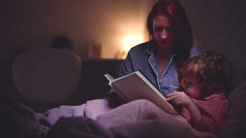 Cheerful mother reading the bedtime stories to toddler baby boy in bed at night Stock Footage