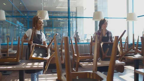 Cheerful multiethnic cafe workers arranging chairs preparing for work in morning Stock Footage 134542695