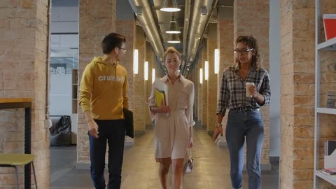 Cheerful Multiethnic Colleagues Walking through Hallway and Chatting Stockbeeldmateriaal 126132331