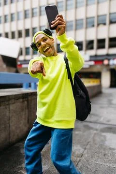 Cheerful multiracial man pointing at camera while taking selfie in city stree Stock Photos