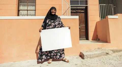 Cheerful Muslim woman holding a blank placard outside her home Stock Photos