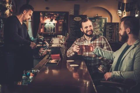 Cheerful old friends drinking draft beer at bar counter in pub. Stock Photos