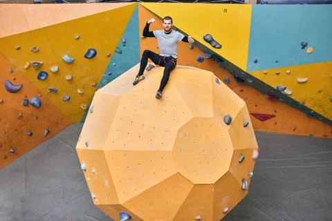 Cheerful physically challenged boulderer sitting on top of large artificial rock Stock Photos