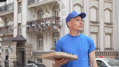 Cheerful pizza courier smiling to the camera after looking around on city street Stock Footage 115170189