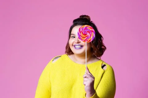 Cheerful plus size model with big lollipop, fat woman in yellow jumper on pin Stock Photos