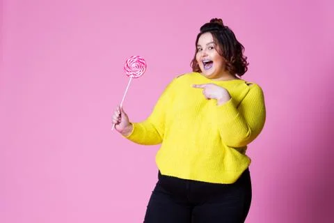 Cheerful plus size model with big lollipop, fat woman in yellow jumper on pin Stock Photos