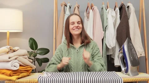 Cheerful positive brown haired young woman wearing knitted shirt ironing clothes 動画素材 259081750