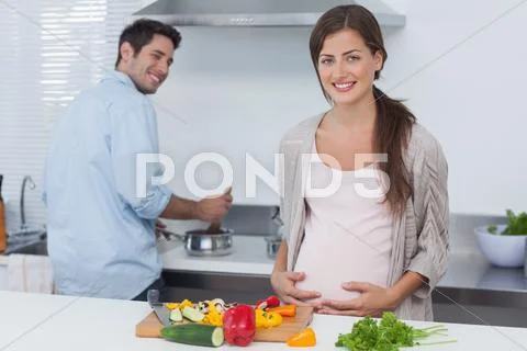 Cheerful pregnant woman holding her belly in the kitchen Stock Photos