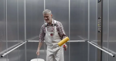 Cheerful professional painter dancing and singing in the elevator Stock Footage 308916320