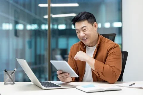 A cheerful programmer enjoys testing an application on a tablet, seated at a Stock Photos